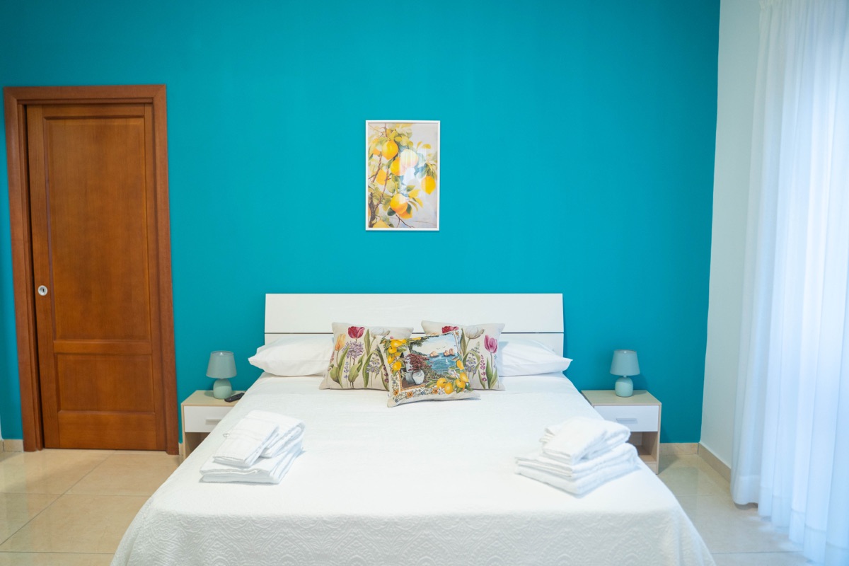 Letto matrimoniale con parete turchese, quadro con limoni e cuscini decorati